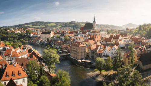 Historische Stadt auf einem grünen Hügel unter blauem Himmel mit weißen Wolken, weite Landschaft im Hintergrund.
